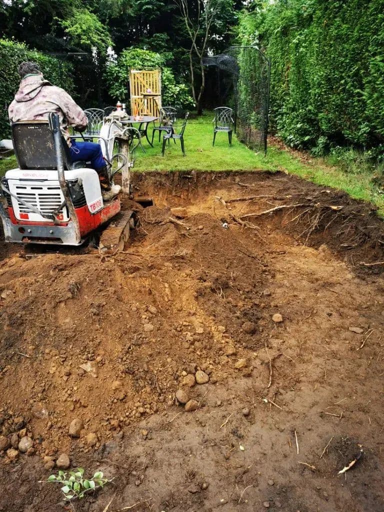 A mini digger cutting into the slope to make a level base for the gazebo