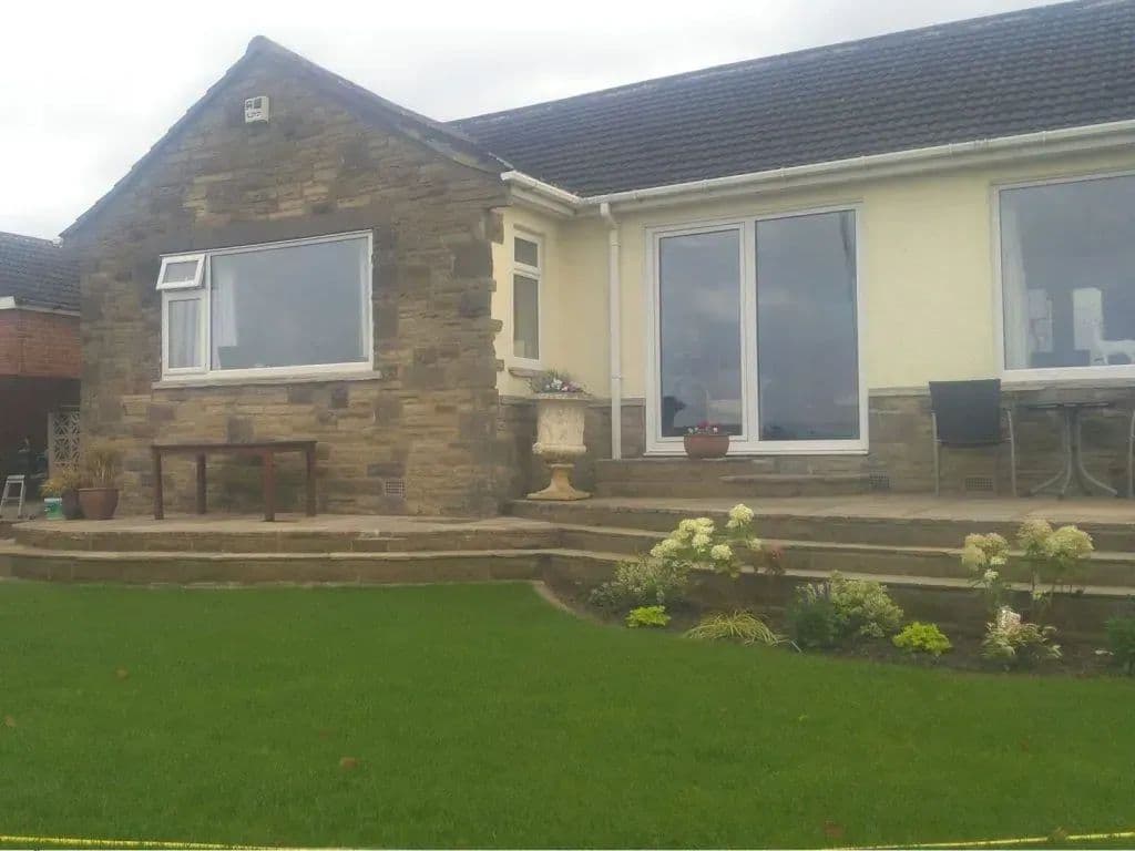 The back of the bungalow with steps down to the lawn and a planted bed alongside