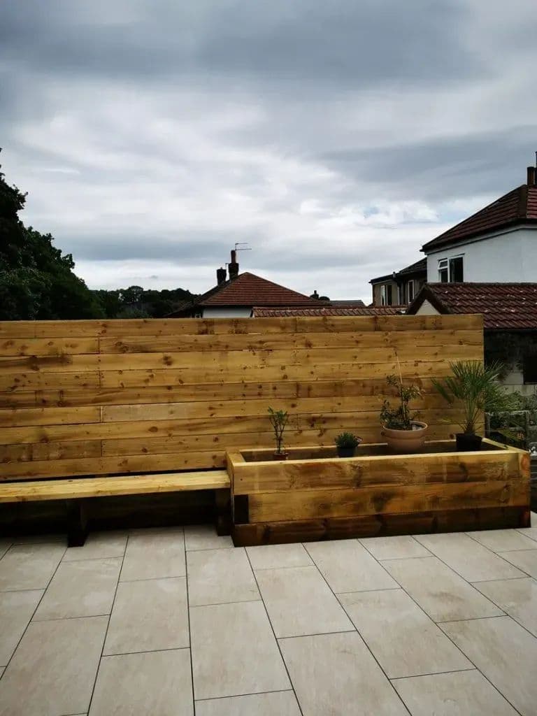 The porcelain-tiled patio with a timber bench and planter running along the boarded wall