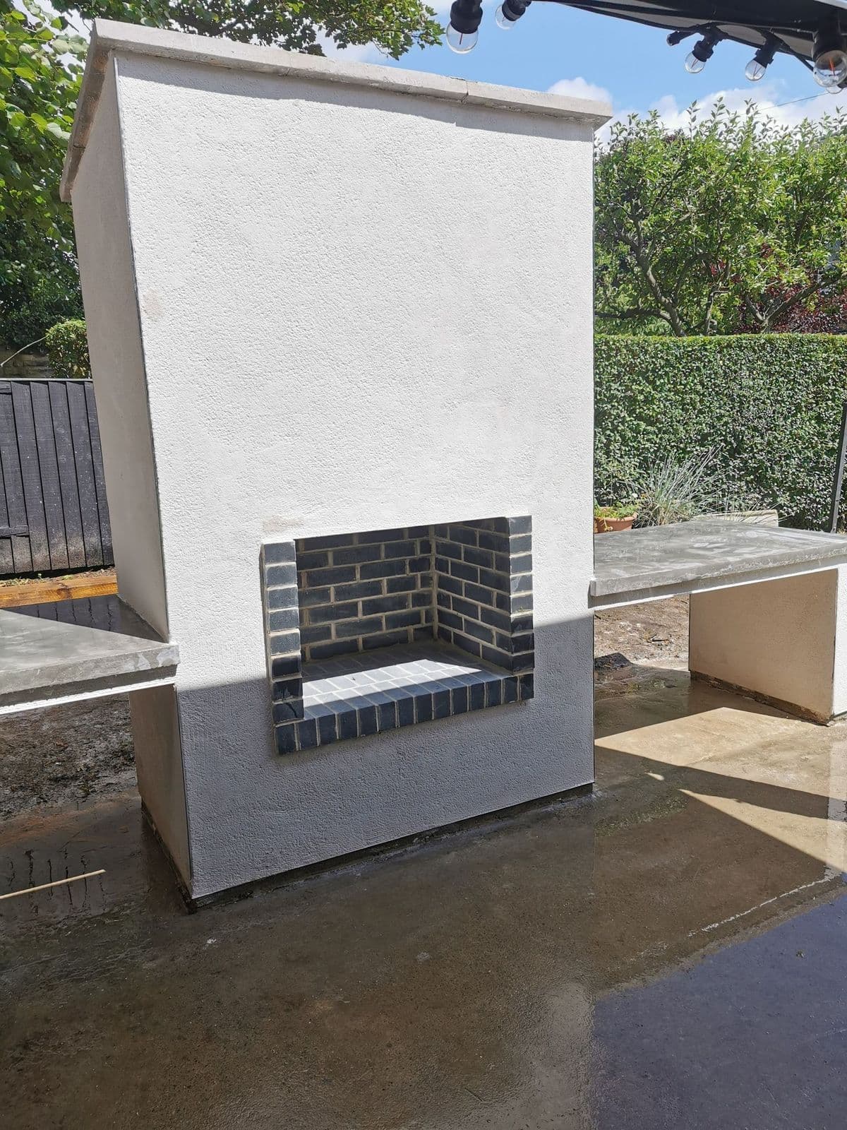 The outdoor oven from the front: a Staffordshire blue brick opening set in chalk white render, with a polished concrete top alongside