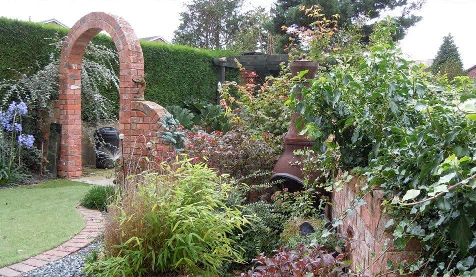 A brick archway in a garden wall with a lawn on one side and deep mixed borders of shrubs and perennials on the other
