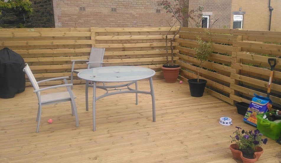 Timber decking with slatted screens, a table, chairs and pots